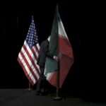 مذاکرات ایران و آمریکا. پرچم ایران توسط فردی از مقابل پرچم آمریکا برداشته می‌شود.